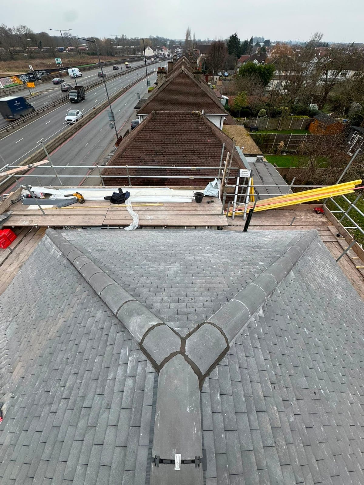 Newly tiled grey hip roof with bedded ridge and hip tiles, scaffold platform at the eaves