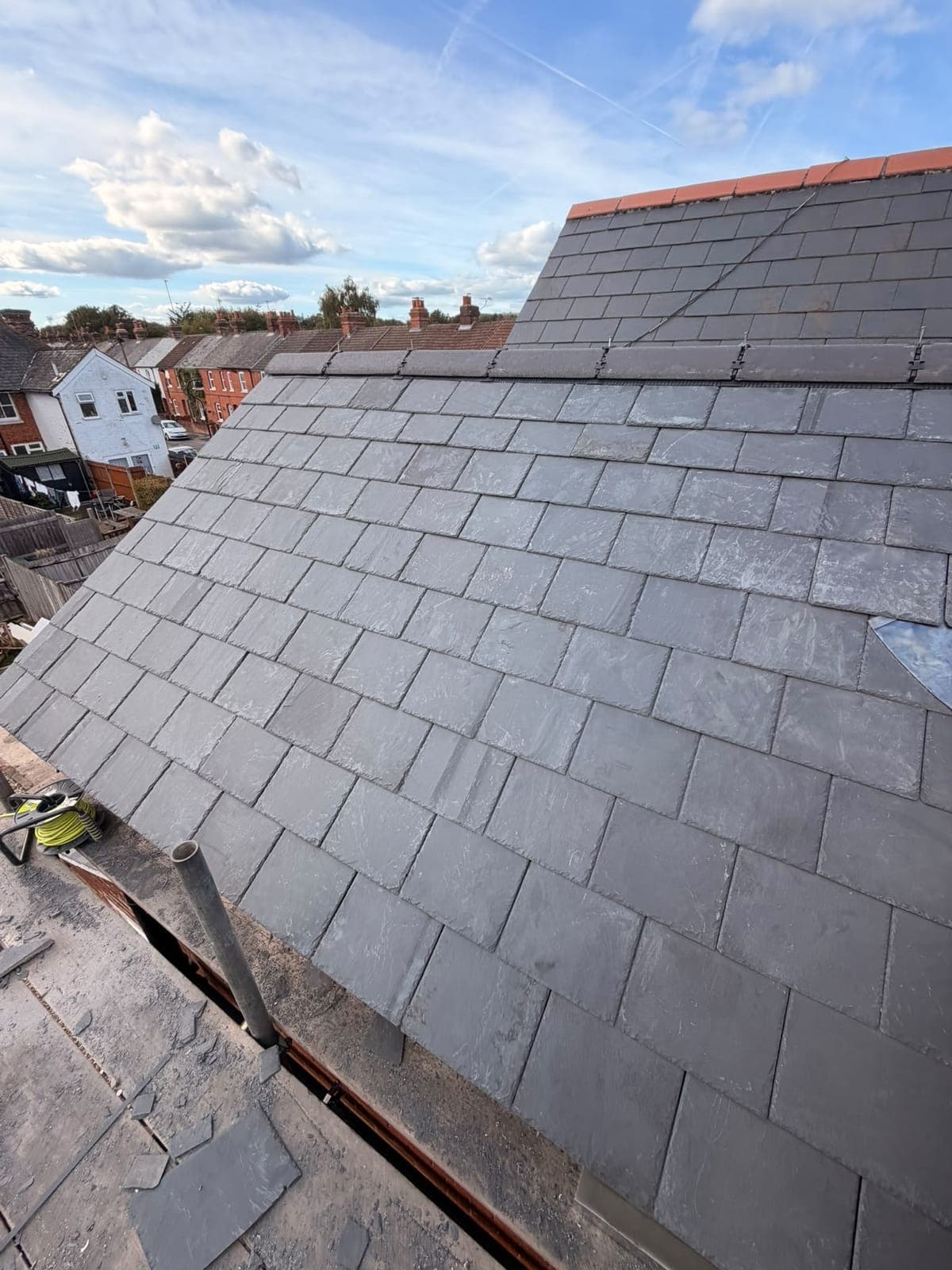 New natural slate roof with clay ridge tiles on a terraced house, with brick chimneys and neighbouring roofs behind